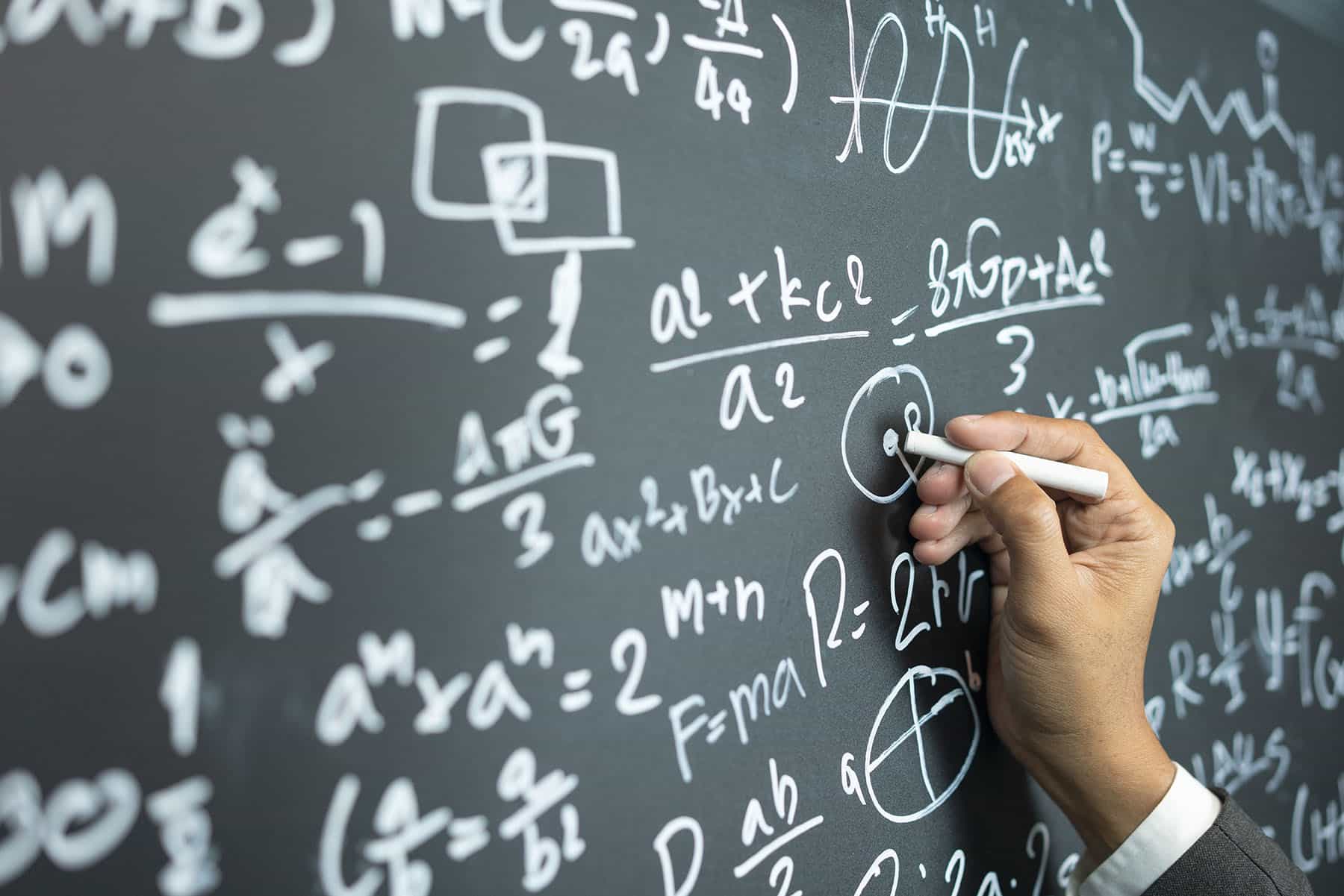 Person writing mathematical equations on a board.